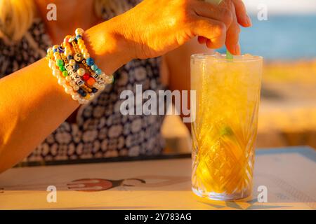 La main d'une dame tient un Sundowner au crépuscule en vacances Banque D'Images