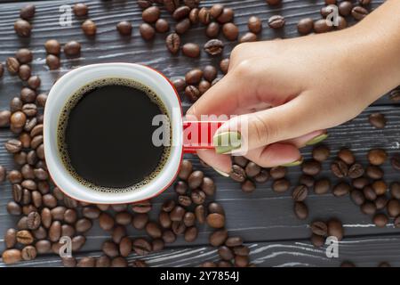 Main féminine tenant une tasse de café sur un fond de grains de café couché sur la table, vue de dessus Banque D'Images