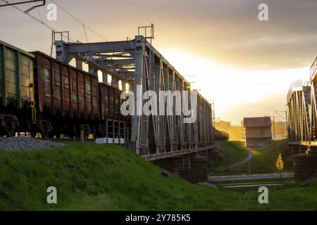 Un pont de chemin de fer sur lequel un train avec des wagons se déplace contre le fond d'un soleil brillant Banque D'Images