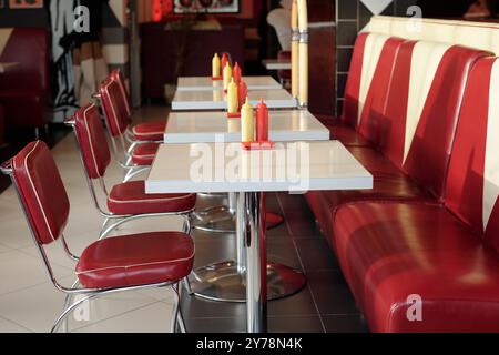 Intérieur du restaurant rétro présentant des rangées de sièges en cuir rouge et des tables blanches avec des bouteilles de condiments sur chaque table, créant une ambiance nostalgique Banque D'Images