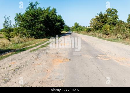 Mauvaise route, asphalte fissuré avec nids de poule et gros trous. La surface asphaltée est détruite sur la route. Mauvais état de la route, a besoin de réparation Banque D'Images