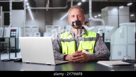 Ouvrier d'usine avec du ruban adhésif noir sur sa bouche dans le bureau Banque D'Images
