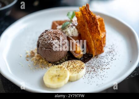 Gaufre à la crème glacée au chocolat servie avec crumble de biscuits, crème fouettée et banane sur l'assiette Banque D'Images