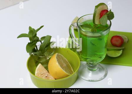 Limonade verte dans un verre. Décoré de citron vert et de fraises. Avec des brins de menthe. Près du citron et de la menthe. Banque D'Images
