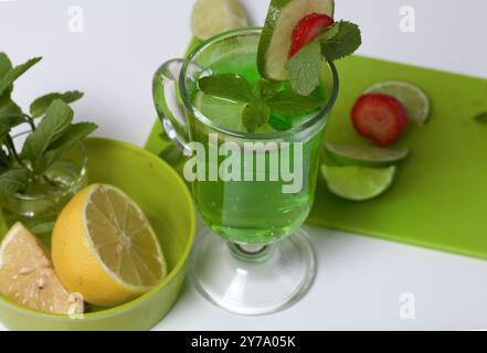 Limonade verte dans un verre. Décoré de citron vert et de fraises. Avec des brins de menthe. Près du citron et de la menthe. Banque D'Images