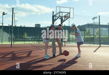 une famille sportive joue au basket-ball, un père, des filles passent du temps libre sur le terrain de basket-ball, mènent un mode de vie sain, une jeune fille lance une balle, Banque D'Images