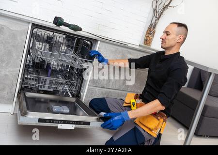 Young Repairman Fixing Dishwasher With Screwdriver In Kitchen Stock Photo