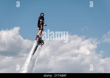 L'homme portant un casque et un gilet de sauvetage vole à l'aide d'un puissant jet d'eau flyboard Banque D'Images