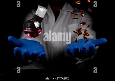 Flacon de chimie à fond rond et pilules transparentes tombant sur une main de scientifique humain avec un espace de copie de fond noir. Chimie médicinale chimie rouge Banque D'Images