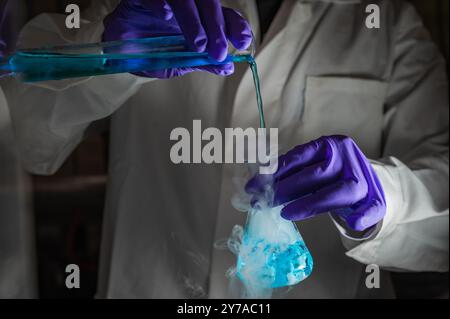 Une femme scientifique effectuant une réaction organique dans des conditions fumantes dans un laboratoire. Fumées, radioactives, fluorescence. Un arrière-plan noir d'espace de copie. Banque D'Images