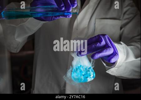 Une femme scientifique effectuant une réaction organique dans des conditions fumantes dans un laboratoire. Fumées, radioactives, fluorescence. Un arrière-plan noir d'espace de copie. Banque D'Images