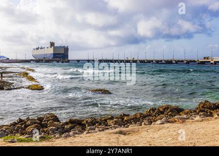 Navire cargo amarré à un quai avec des vagues frappant la rive rocheuse et le ciel nuageux, situé sur la côte de l'île de Curaçao dans la mer des Caraïbes. Banque D'Images