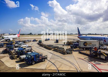 Tarmac d'aéroport occupé à l'aéroport international de Miami avec des avions d'American Airlines desservis par des véhicules terrestres et l'équipage sous le ciel ensoleillé. Miami. Banque D'Images