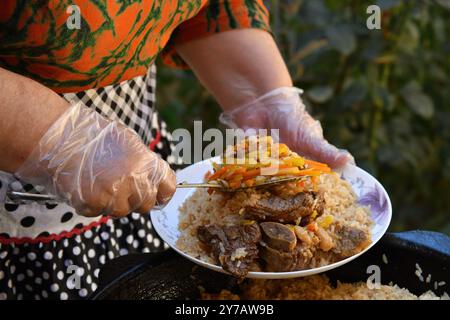 Cuisine orientale traditionnelle ouzbèke, pilaf ou plov avec de gros morceaux de viande et des carottes, cuite dans une poêle en fonte noire de kazan. Mise au point sélective Banque D'Images