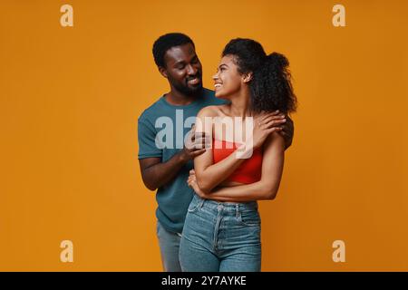 Beau jeune couple africain souriant et embrassant tout en se tenant debout sur fond jaune Banque D'Images