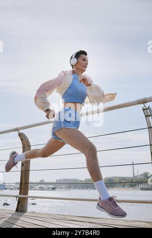 Plan vertical d'une femme mature courant vite sur le front de mer, elle écoutant de la musique tout en faisant du cardio Banque D'Images
