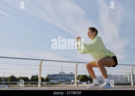Jeune adulte caucasien habillé en vêtements de sport d'été faisant des squats sur le front de mer Banque D'Images