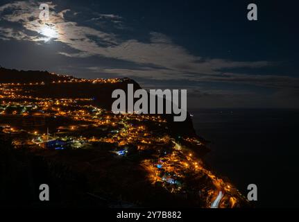 Arco Da Calheta, Portugal. 18 septembre 2024. La lune et les nuages légers peuvent être vus au-dessus du village, qui est illuminé la nuit. Le village au sud-ouest de l'île a été fondé au XVe siècle et doit son nom aux montagnes environnantes. Crédit : Soeren Stache/dpa/Alamy Live News Banque D'Images