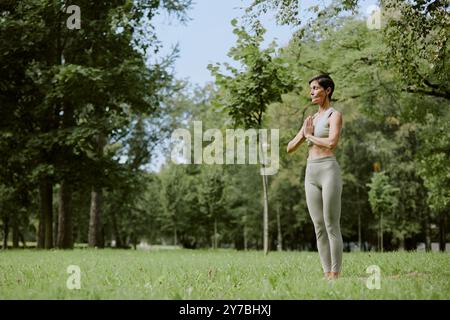 Femme caucasienne senior médiatrice dans un parc verdoyant, elle se tenait immobile sur une pelouse verte et immergée dans les pensées Banque D'Images