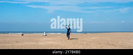 wijk aan zee, pays-bas, 7 septembre 2024 : femme marche vers la mer en transportant une planche de surf sur la plage aux pays-bas Banque D'Images