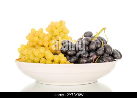 Deux grappes de raisins mûrs blancs et noirs dans un plat en céramique, macro, isolé sur fond blanc. Banque D'Images