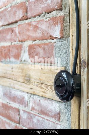 Interrupteur électrique vintage, bouton lumineux avec câble électrique noir monté sur un mur à colombages ou à ossature de bois. Banque D'Images