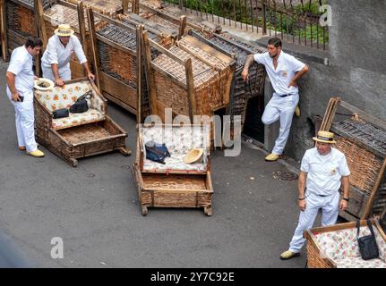 19 septembre 2024, Portugal, Funchal : les conducteurs vêtus de blanc des traîneaux à nacelles en bois attendent les passagers près de la station de montagne Monte du téléphérique. Dès le 19ème siècle, les habitants de la commune de Monte, qui se trouve à 500 mètres d'altitude, utilisaient les traîneaux comme moyen de transport public pour se rendre plus rapidement à la ville de Funchal. Aujourd'hui, les wagons, fabriqués par des artisans de saule et de bois, sont chacun conduits par deux carreiros sur une distance d'environ deux kilomètres dans la vallée jusqu'à Livramento. Les conducteurs freinent pendant la descente avec les semelles en caoutchouc très épaisses de Banque D'Images