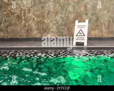 Une plaque de métal attention, sol humide se dresse à côté de la piscine jacuzzi dans un spa moderne, espace copie. Banque D'Images