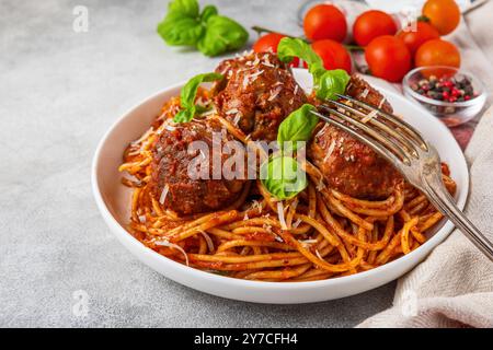 Spaghetti aux boulettes de viande dans une sauce tomate, garni de parmesan et de feuilles de basilic frais dans une assiette avec fourchette sur fond de béton gris Banque D'Images