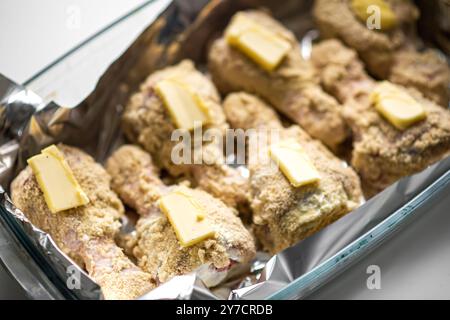 Pilons de poulet panés cuits au four avec beurre sur papier d'aluminium dans un plat allant au four. Banque D'Images