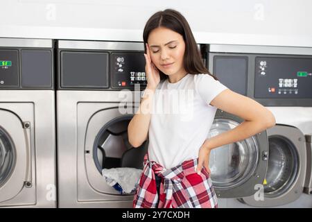Femme dans la laverie montrant la frustration tout en faisant la lessive dans l'après-midi Banque D'Images