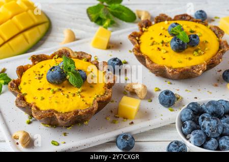Cheesecakes crus végétaliens à la mangue jaune avec bleuets frais, pistaches et menthe. Délicieuses tartes sans gluten saines. Gâteau végétalien. Dessert sans sucre Banque D'Images