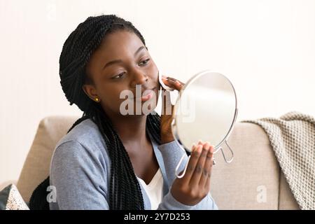 Fille noire à la recherche de miroir et visage nettoyage avec un coton Banque D'Images