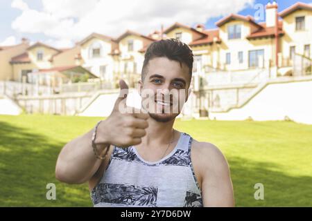 L'homme au repos attrayant avec thumb up. Belles chambres d'hôtes dans l'arrière-plan Banque D'Images