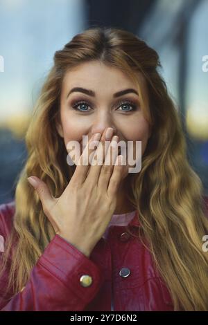 Closeup portrait of belle blonde pensive white Caucasian girl femme, portée à l'extérieur de red jacket in city street, style portrait concept Banque D'Images