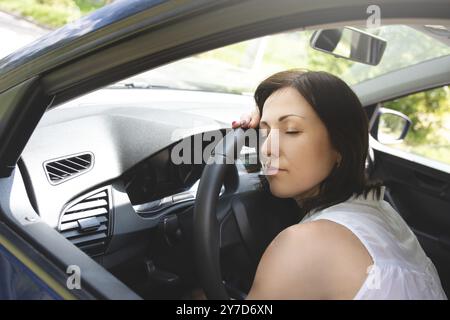 Femme fatiguée endormie sur le volant dans sa voiture Banque D'Images