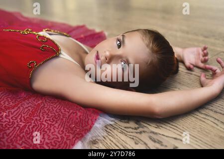 Portrait vue de côté d'une jolie belle petite ballerine dans une robe de performance couchée sur le sol de la salle de danse Banque D'Images