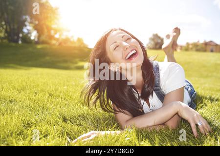 Vacances d'été, femme adulte détendue allongée sur l'herbe verte dans un parc en plein air. fille dans des lunettes de soleil appréciant la nature couchée sur l'herbe Banque D'Images