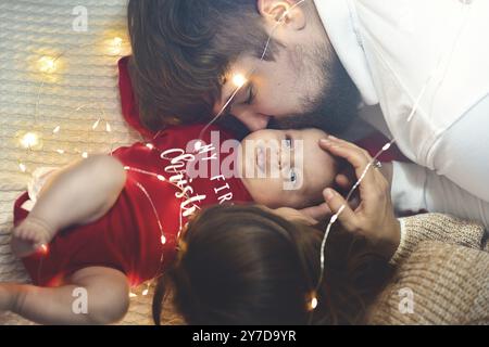 Vue de dessus. Mère et Père embrasse bébé au lit. Petit enfant nouveau-né dans un lit blanc. Concepts de parentalité. Amour et bonheur. Prendre soin d'une nouvelle vie Banque D'Images