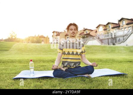 Jeune homme méditant à l'extérieur dans le parc, assis avec les yeux fermés et les mains Banque D'Images