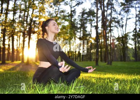 Une jeune femme pratique la méditation dans une forêt sereine au lever du soleil, favorisant la paix et la pleine conscience Banque D'Images
