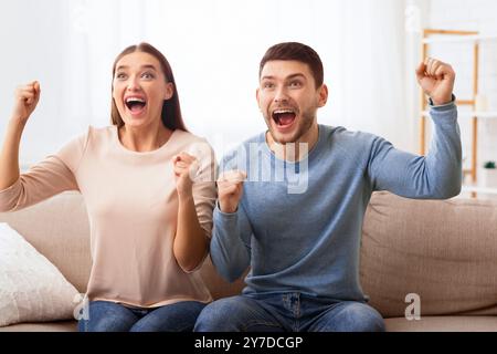 Couple Excité Regardant Les Sports À La Télévision Criant Assis Sur Canapé Banque D'Images