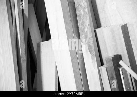 Des planches de bois de différentes tailles sont empilées dans un atelier de charpentier, montrant les matières premières du travail du bois. - noir n blanc - Banque D'Images