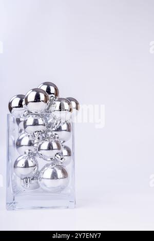 Un vase en verre débordant de boules de Noël argentées de différentes tailles. Les ornements brillants sont disposés comme décor de vacances, sur un fond blanc simple Banque D'Images
