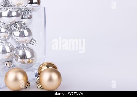 Un arrangement chic avec un vase en cristal débordant de boules argentées de différentes tailles, jumelé avec des ornements dorés brillants sur un fond blanc Banque D'Images