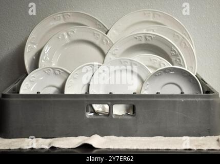 Photographie de plats blancs, assiettes et soucoupes séchant à l'air sur un panier de lave-vaisselle dans une cuisine Banque D'Images