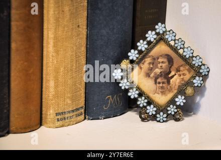 Photographie d'un petit cadre de fleur bleue qui tient un portrait antique de quatre femmes. Derrière eux se trouvent de vieux livres sur une étagère. Banque D'Images