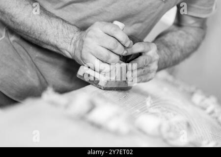 Carpenter lisse une planche de bois à l'aide d'un avion à main traditionnel dans son atelier. - noir n blanc - Banque D'Images