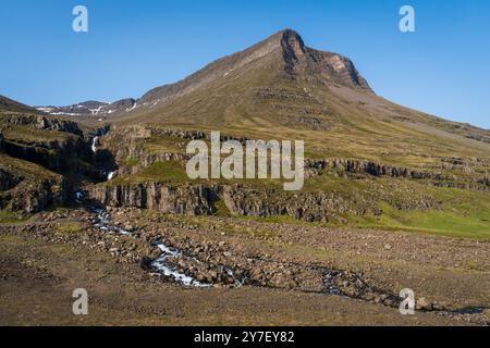 Une petite cascade dévale la base d'un sommet montagneux en forme de pyramide en Islande. Banque D'Images