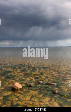 Des nuages sombres se dressent sur le lac Vänern, projetant des ombres sur les eaux tranquilles et le rivage rocheux. L'atmosphère suggère une tempête qui approche, en s'améliorant Banque D'Images